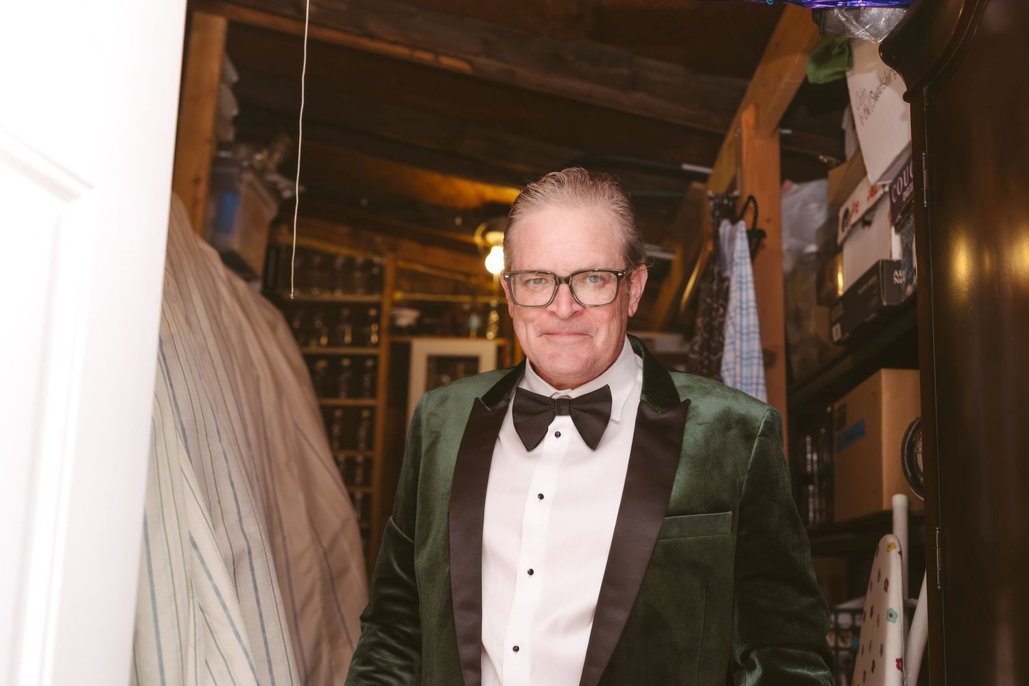 Man in elegant green velvet tuxedo with black bow tie standing in a dimly lit room.