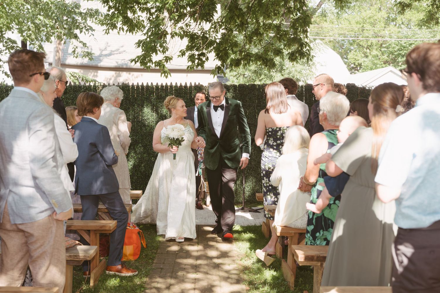 Bride and groom walk back down the aisle after outdoor wedding ceremony surrounded by cheering guests.