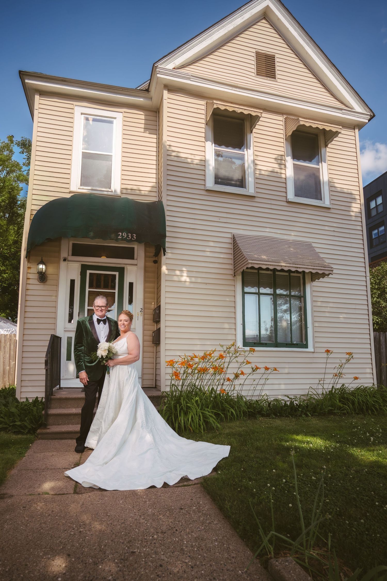 Bride and groom pose together in front of a charming two-story house on their wedding day.