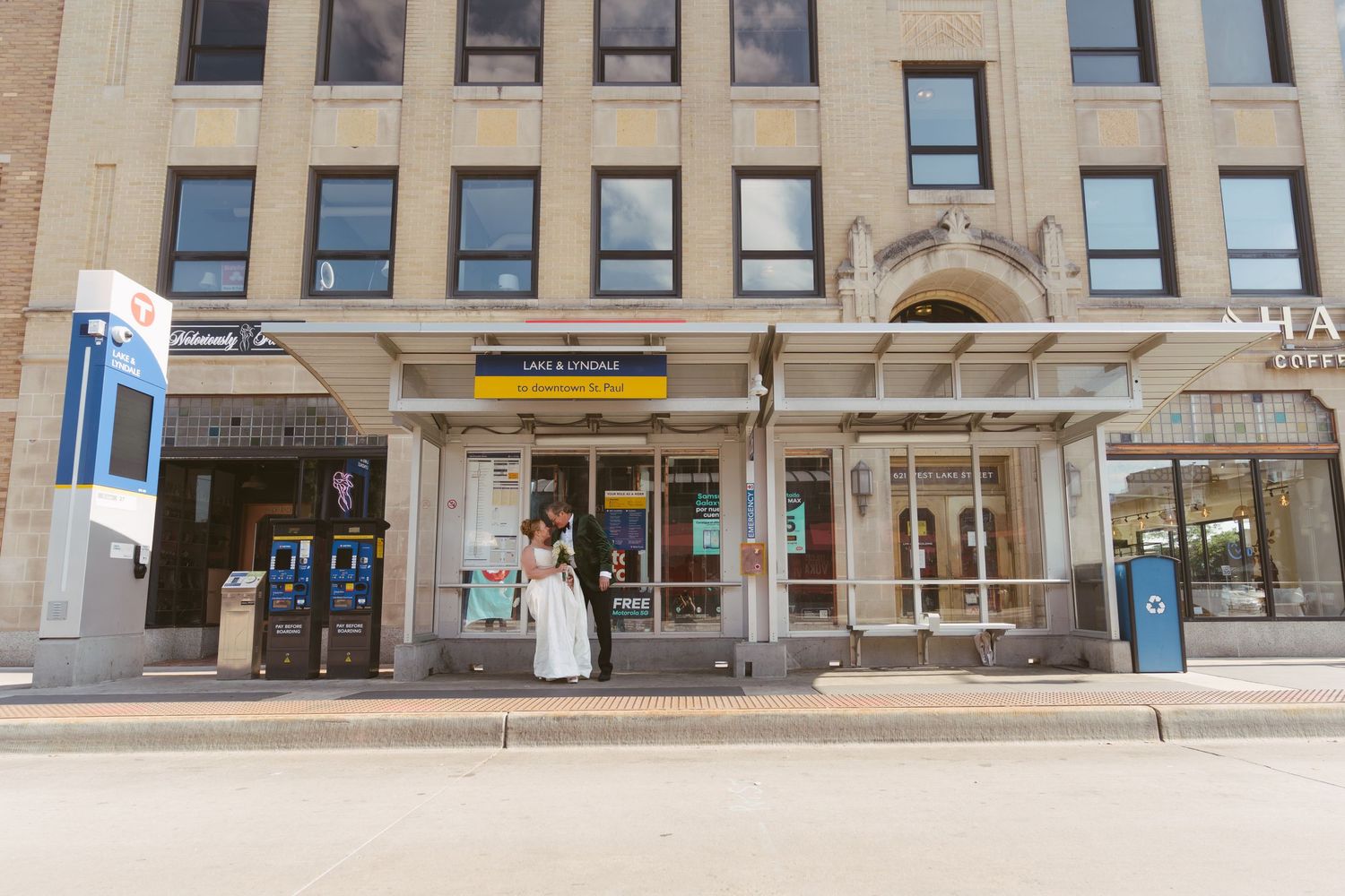 A bride and groom share a kiss outside a urban building on a sunny city street.