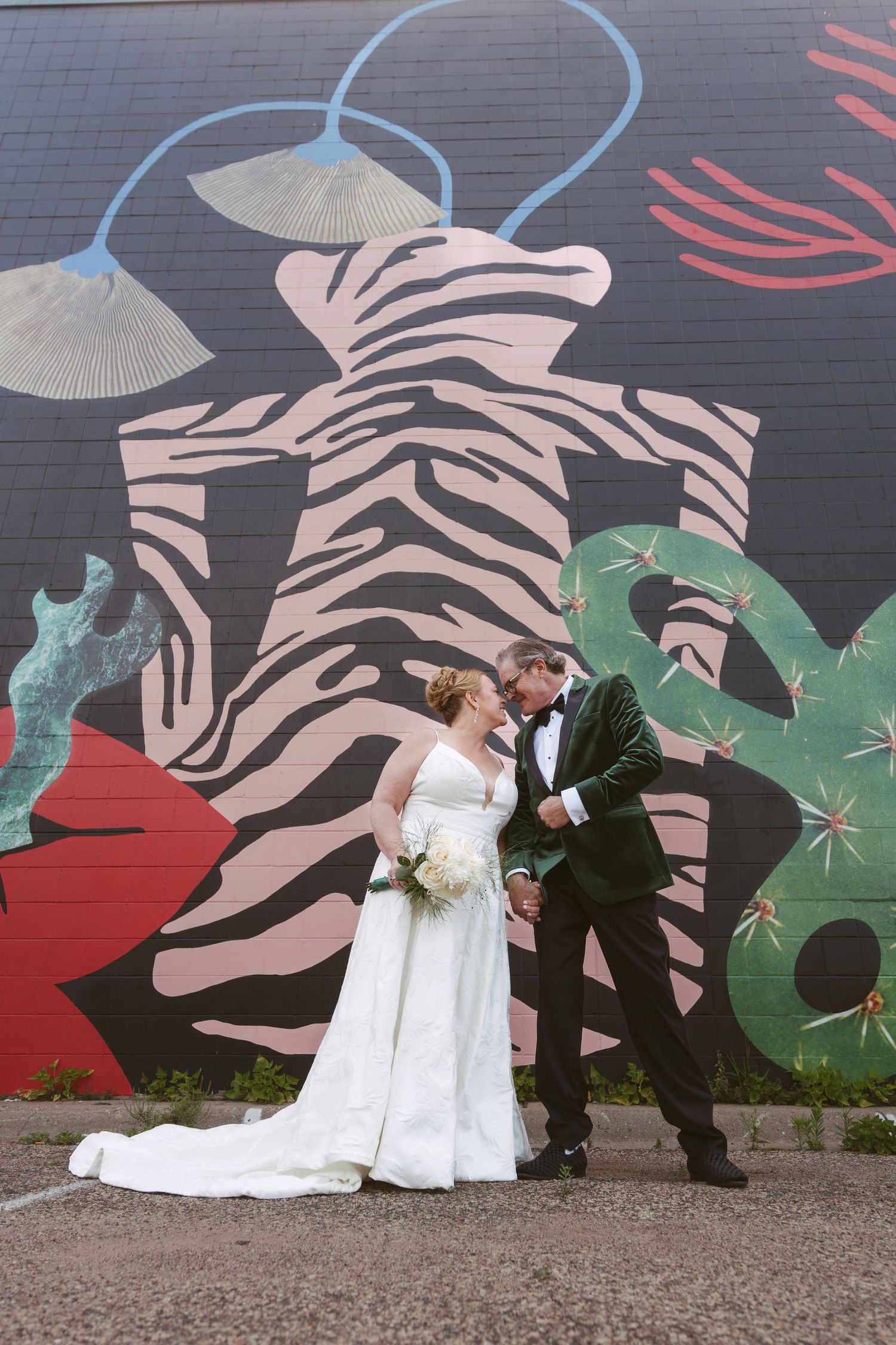 Bride and groom posing romantically in front of a vibrant colorful mural on a city building.