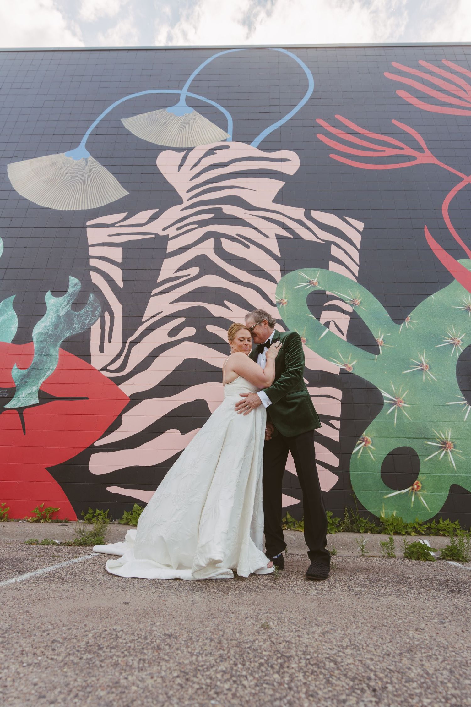 Bride and groom embrace romantically in front of a vibrant colorful street mural featuring abstract zebra artwork.