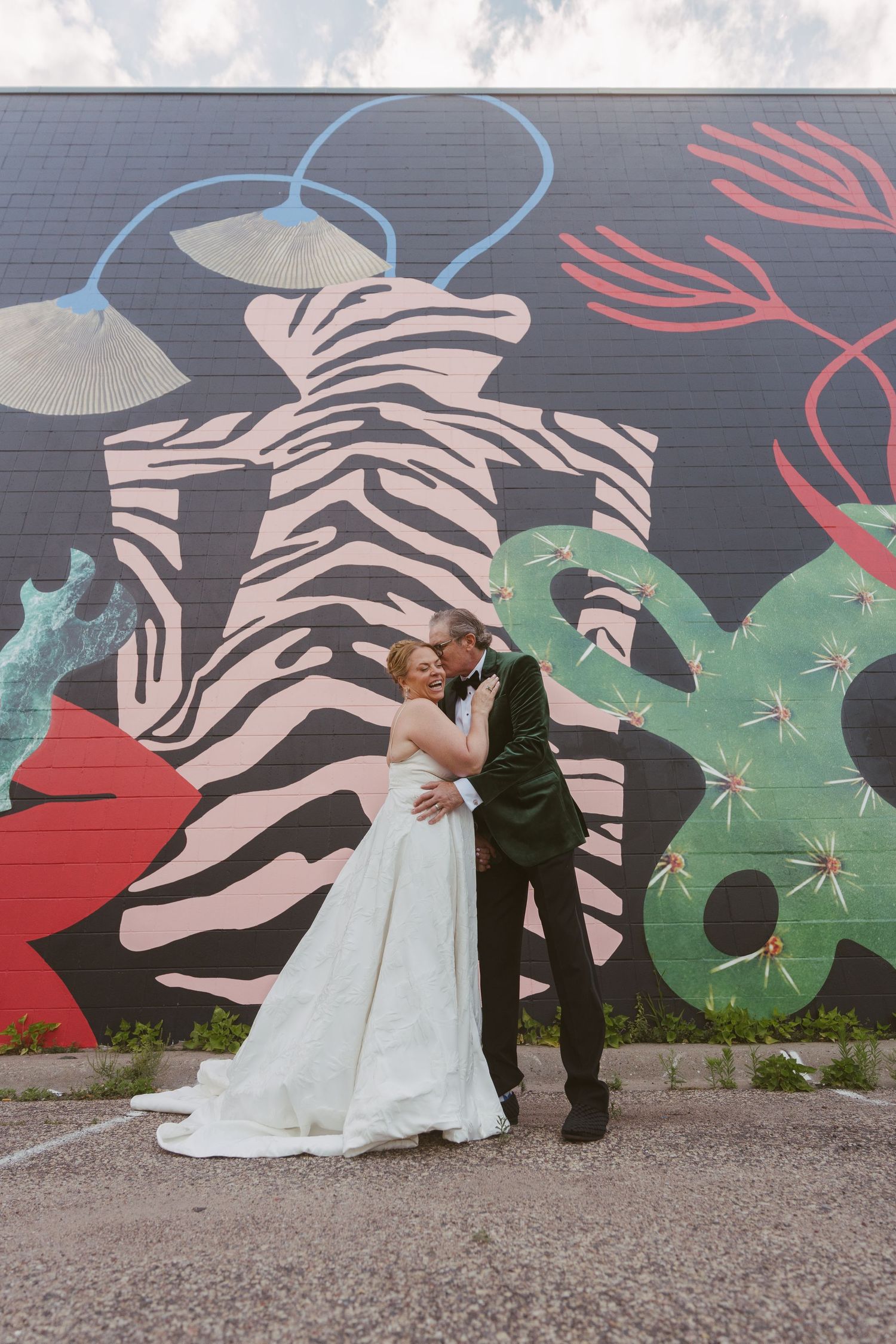 Bride and groom kiss in front of vibrant zebra and cactus street mural outdoors.