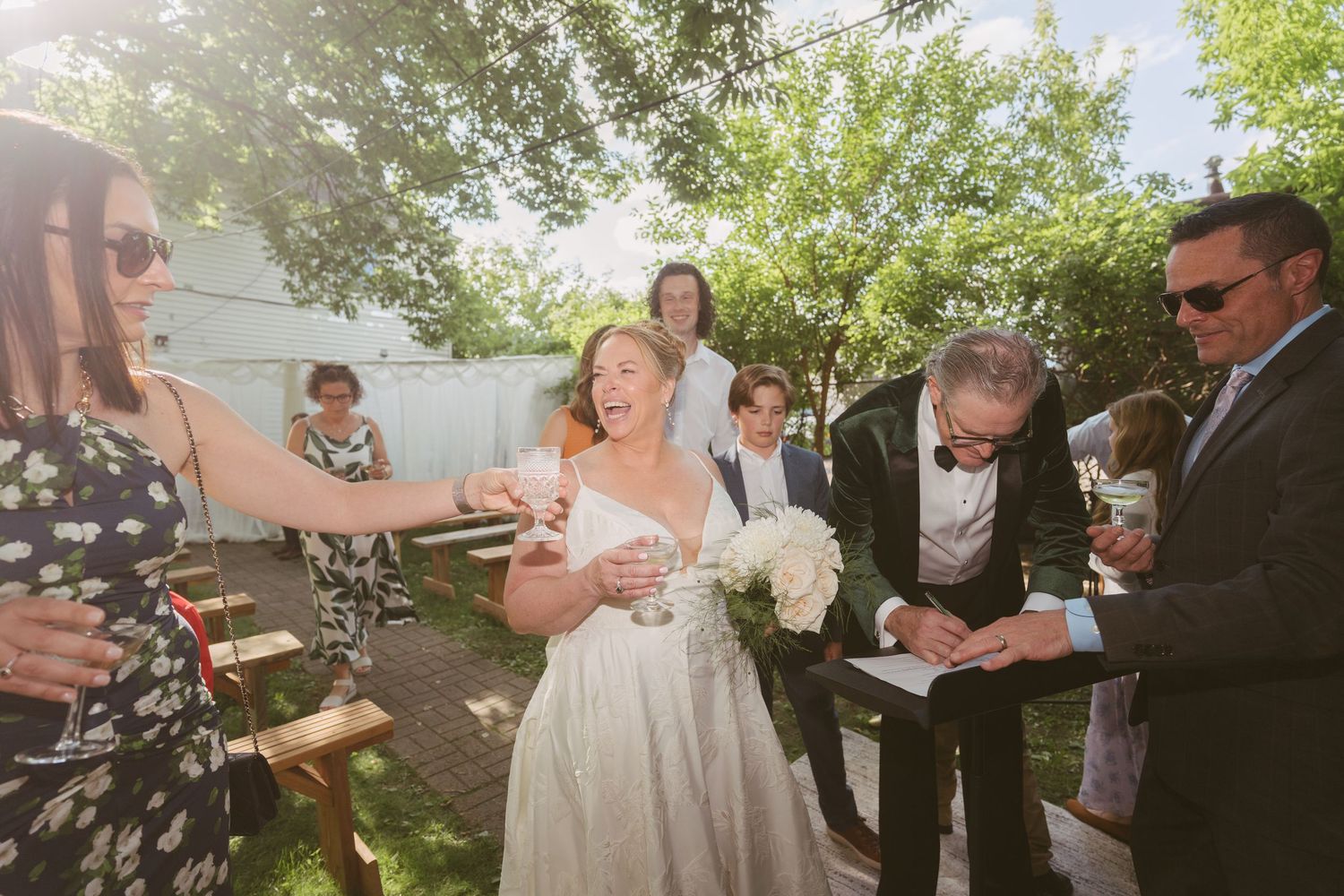 A bride in white receives congratulations from guests during an outdoor backyard wedding ceremony.
