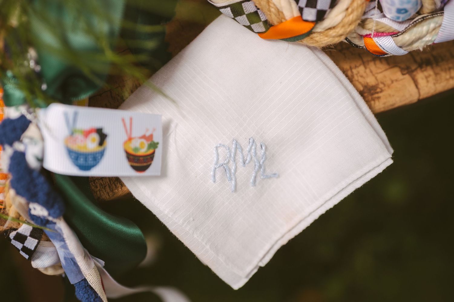 White monogrammed handkerchief with blue embroidered initials displayed at a colorful outdoor celebration.