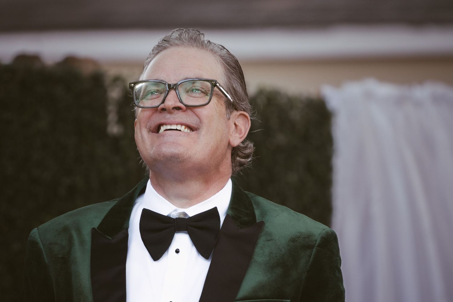 Man in green velvet tuxedo smiling joyfully outdoors at a formal evening event.