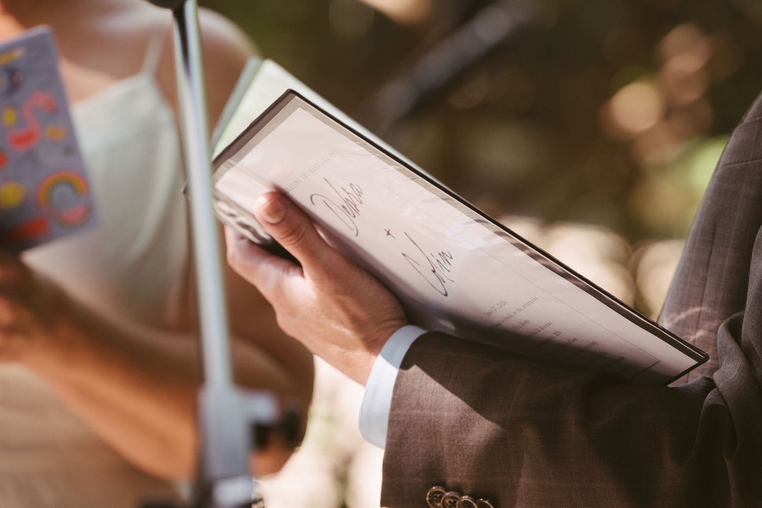 Close-up of hands holding an open book with handwritten notes at a wedding ceremony.