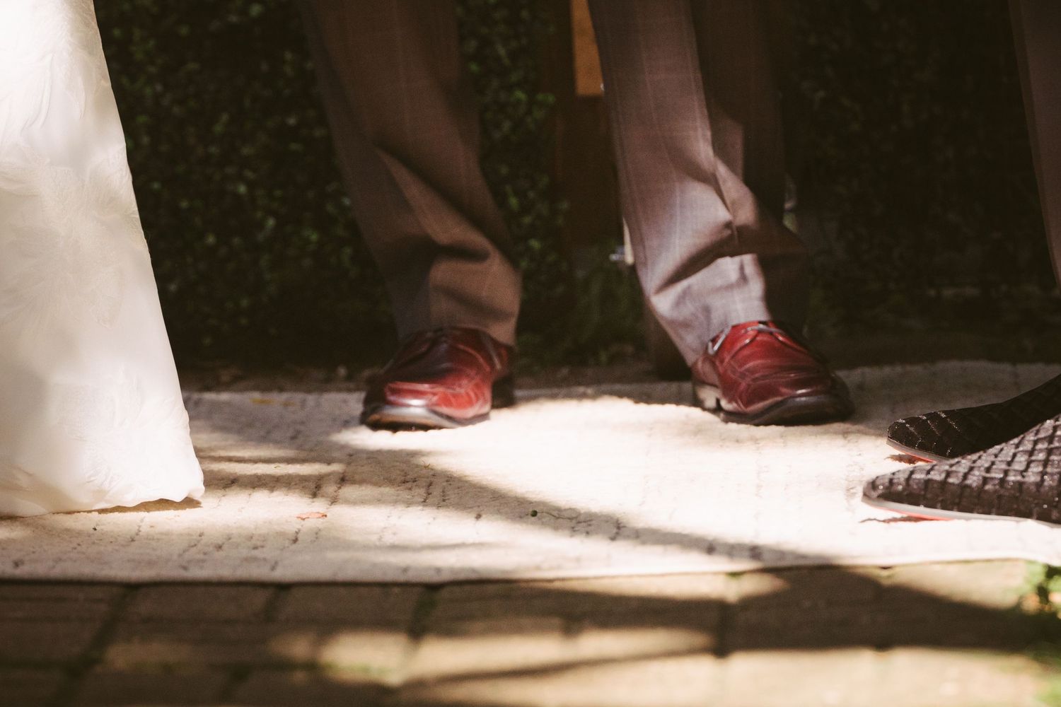 Close-up of wedding guest feet in red sneakers standing on sunlit stone pavement during ceremony.
