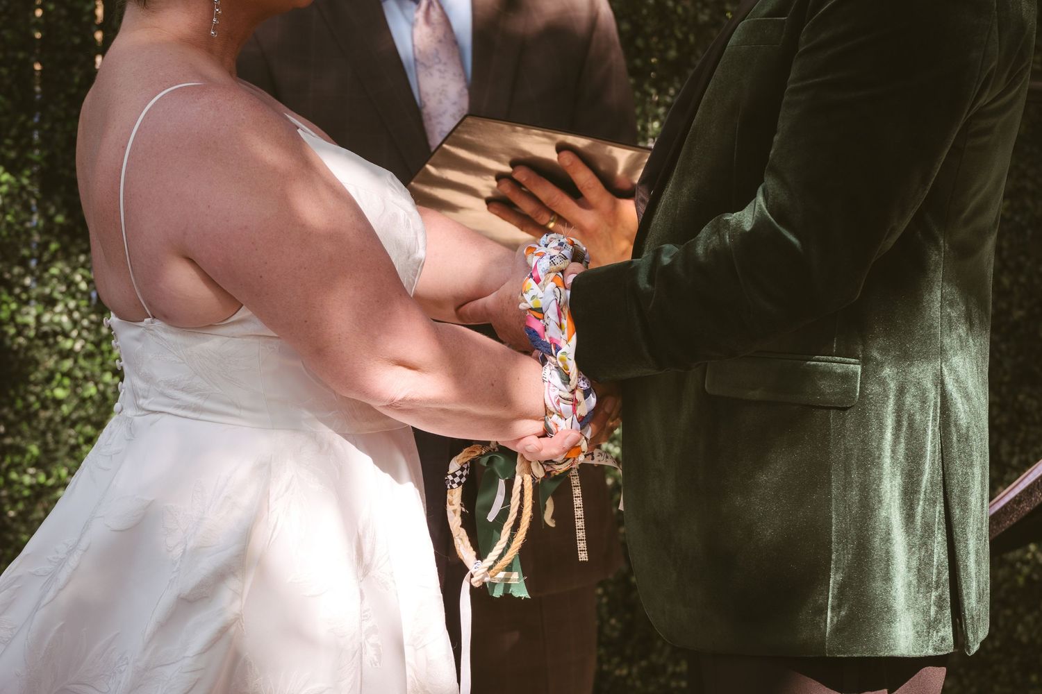 Bride and groom perform handfasting ceremony with colorful ribbons tied around their hands.