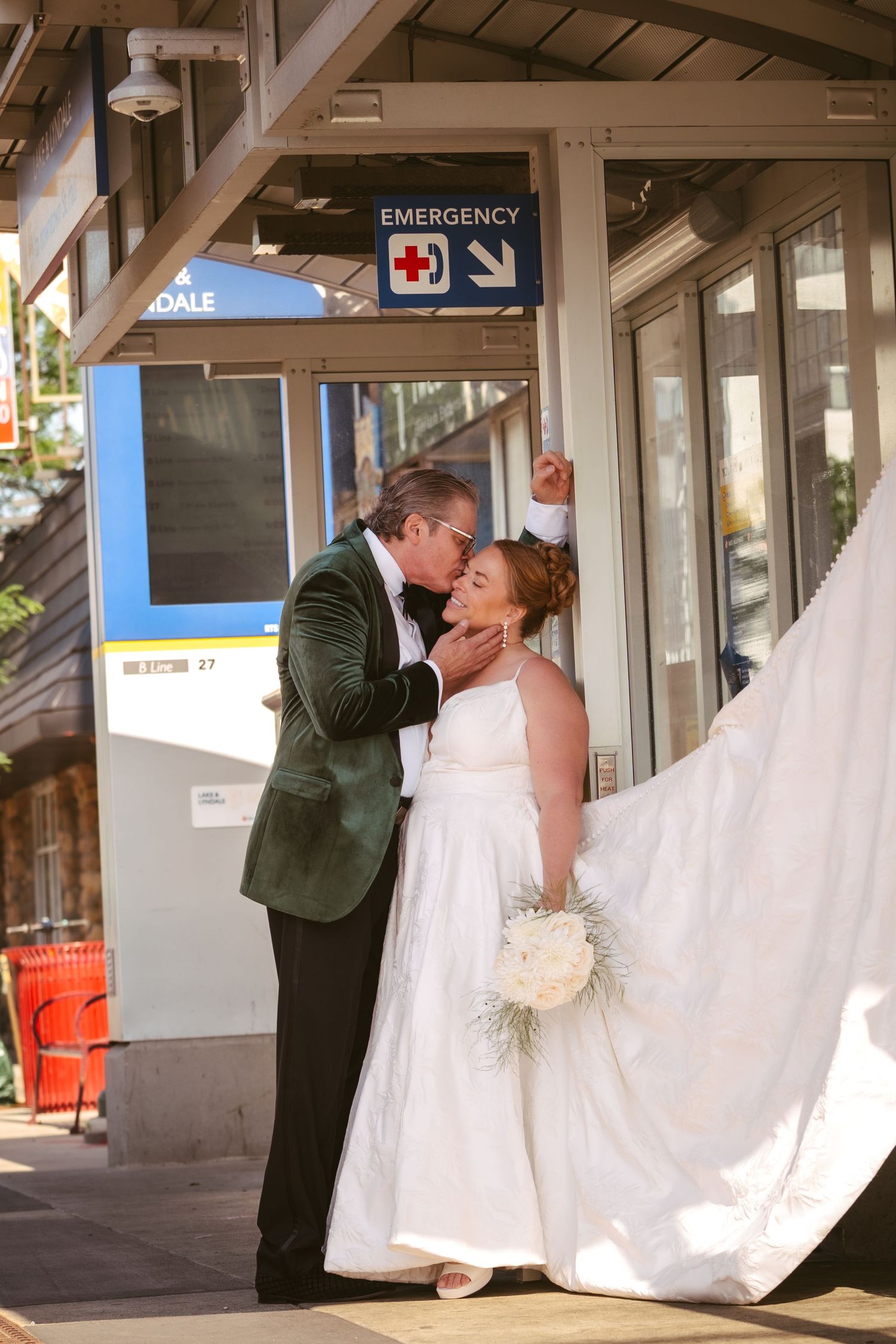 Bride and groom share a kiss outside an emergency entrance at a transit station on their wedding day.