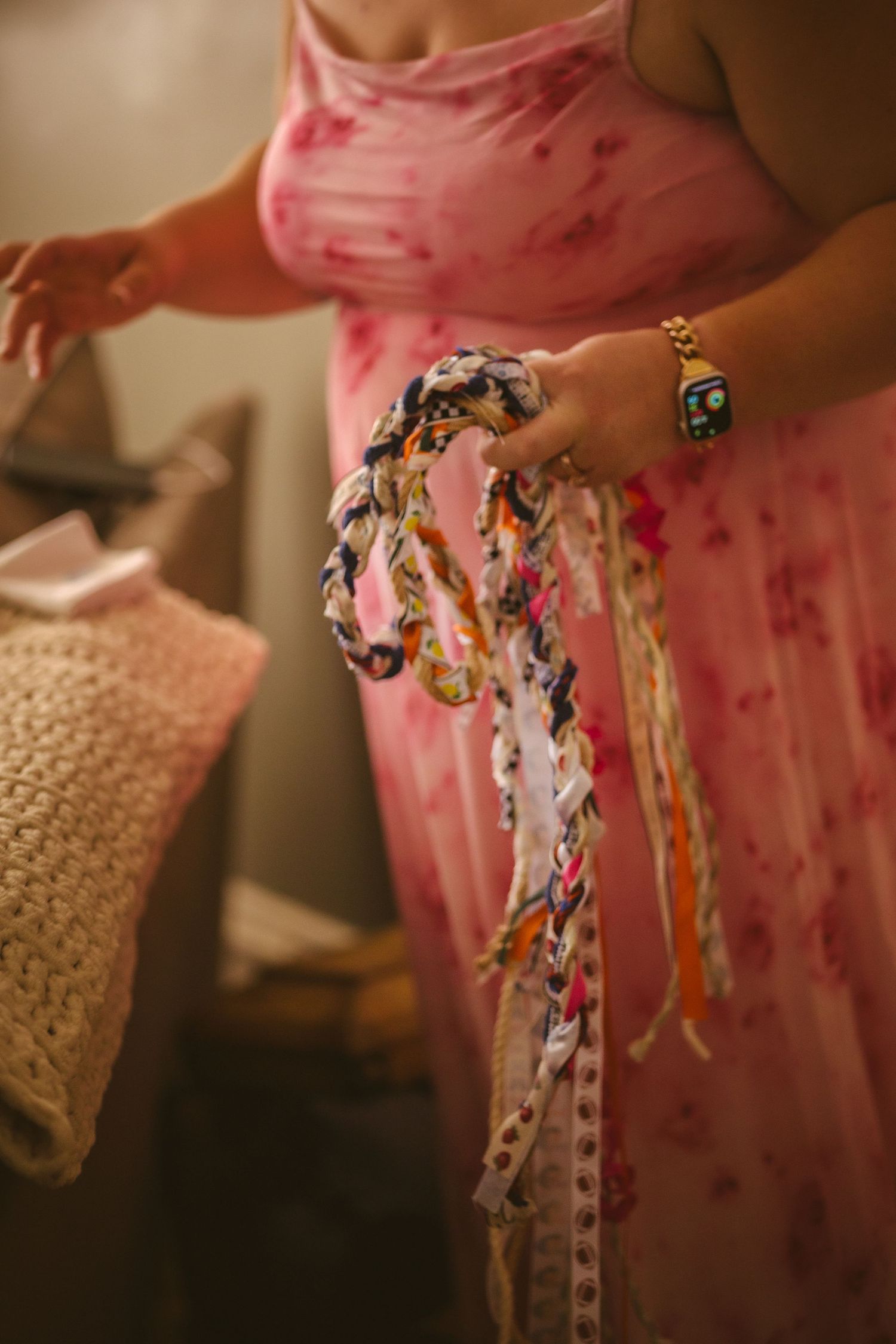 Bride in pink dress holds colorful braided fabric ribbons for handfasting wedding ceremony.