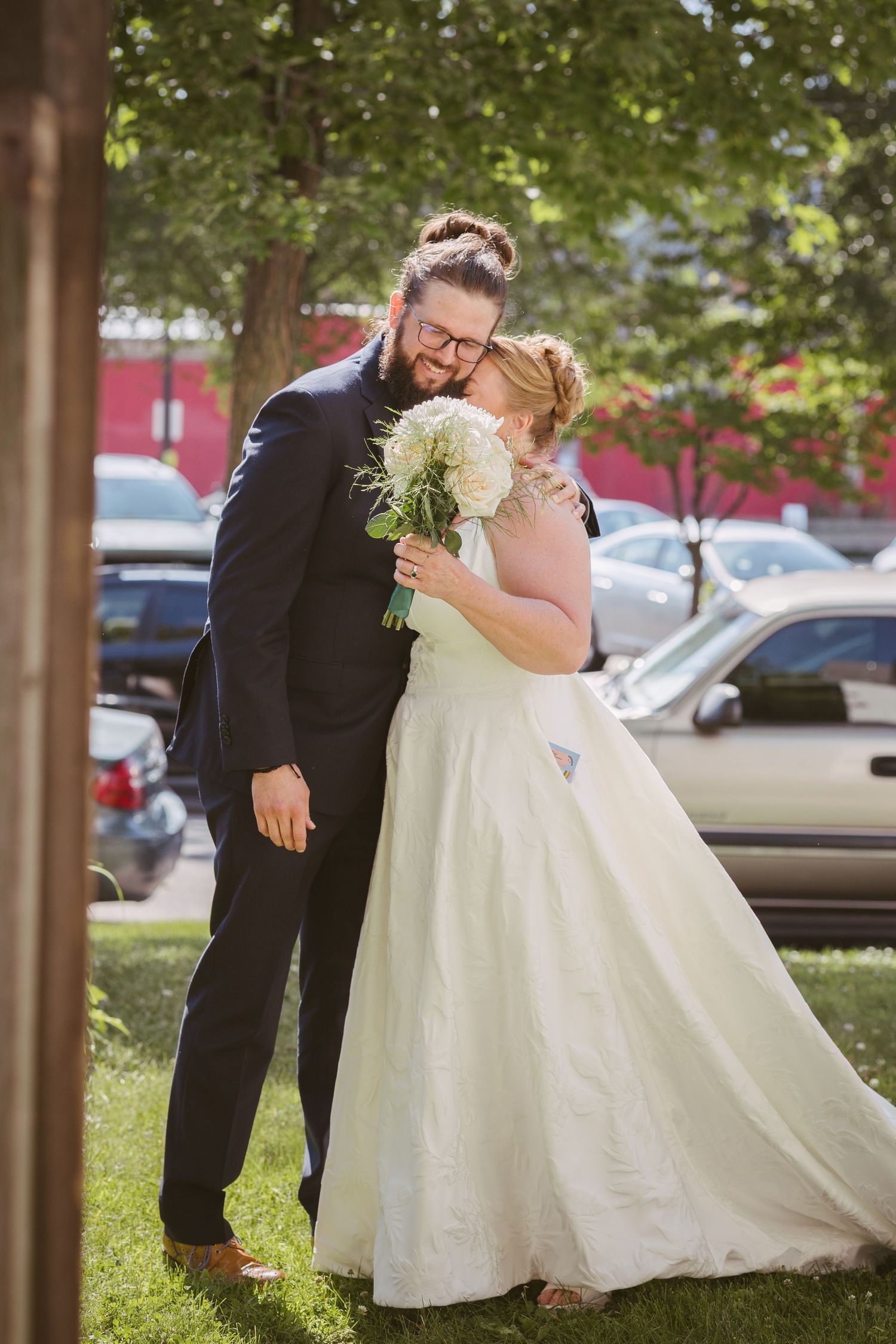 Bride and groom sharing a tender embrace outdoors, bride holding white bouquet in elegant wedding gown.