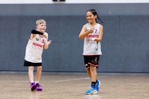 Two young girls in Hornets basketball uniforms smiling during a youth basketball game.