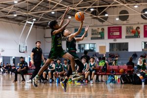 Two youth basketball players compete for a layup shot during an indoor game on a hardwood court.