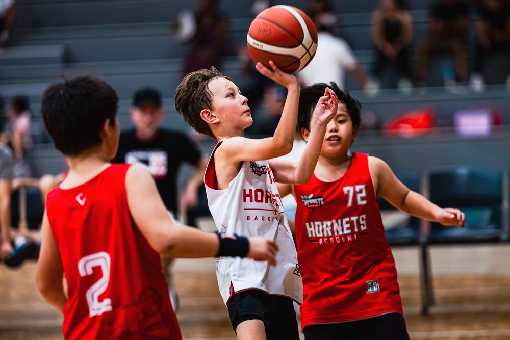 Young basketball player in white Hornets jersey attempts a layup during an indoor youth basketball game.