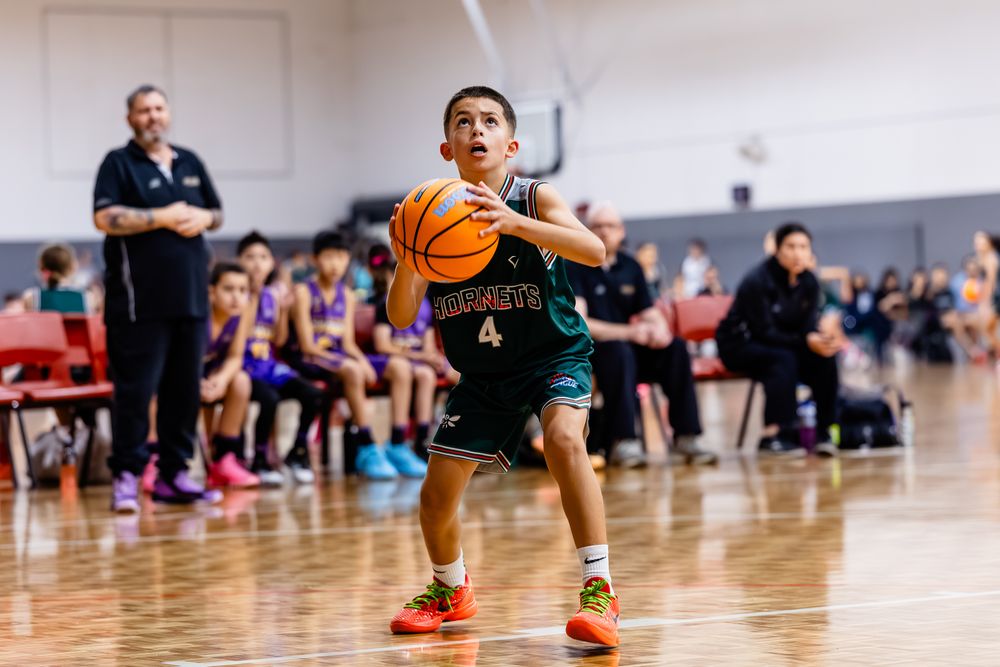 Young boy wearing number 4 jersey dribbling basketball during indoor youth basketball game.