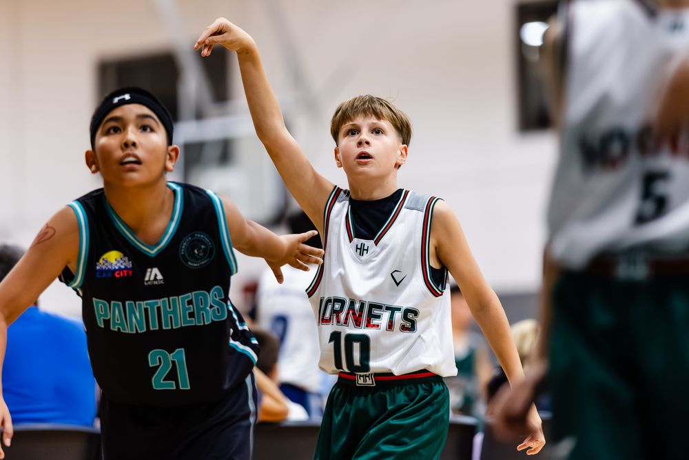 Youth basketball players from Panthers and Hornets teams compete during an indoor junior basketball game.