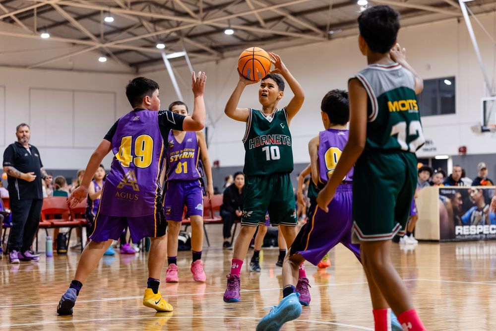 Youth basketball players in green and purple uniforms compete during an indoor game, with player number 10 preparing to shoot.