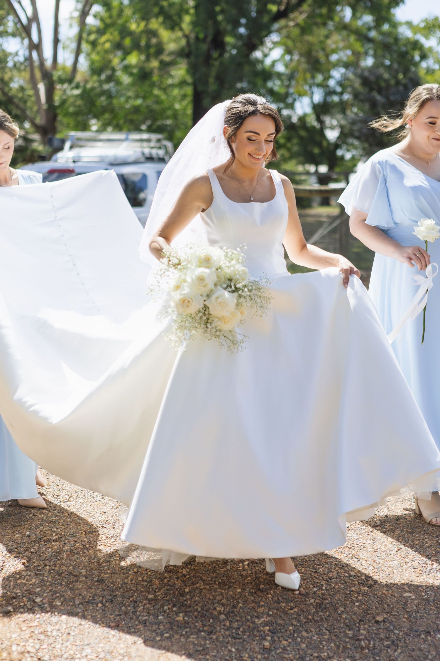 Bride and bridesmaids in blue dresses smiling while walking and holding brides dress at Two Rivers Winery Wedding in Denman