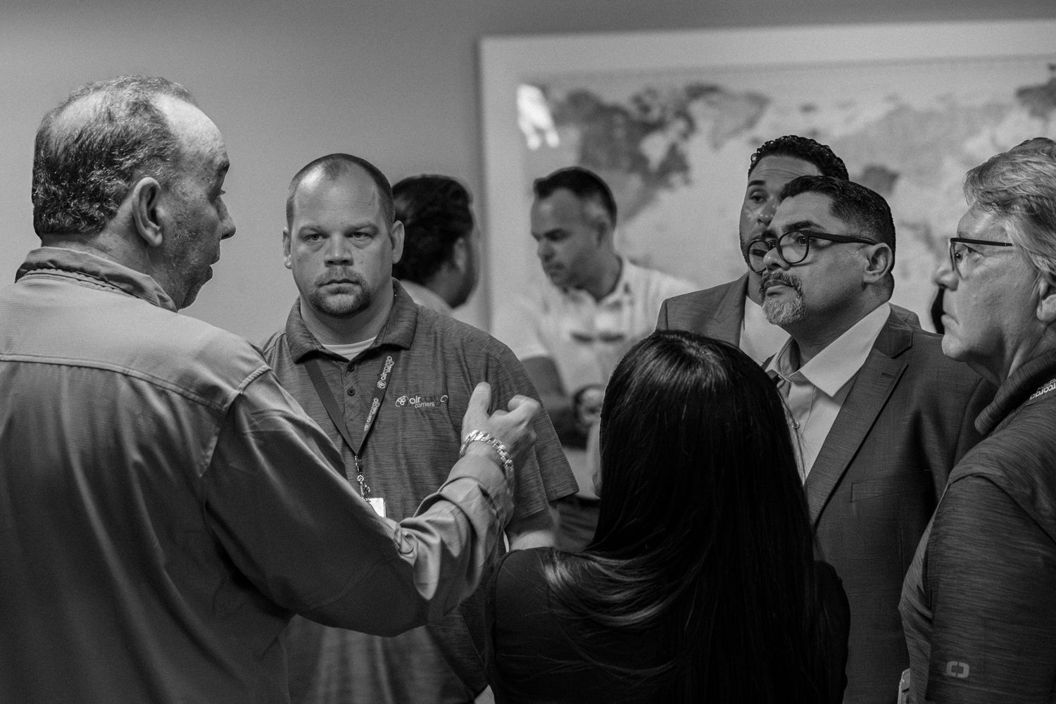 Group of professionals in business casual attire shake hands and converse in black and white photo.