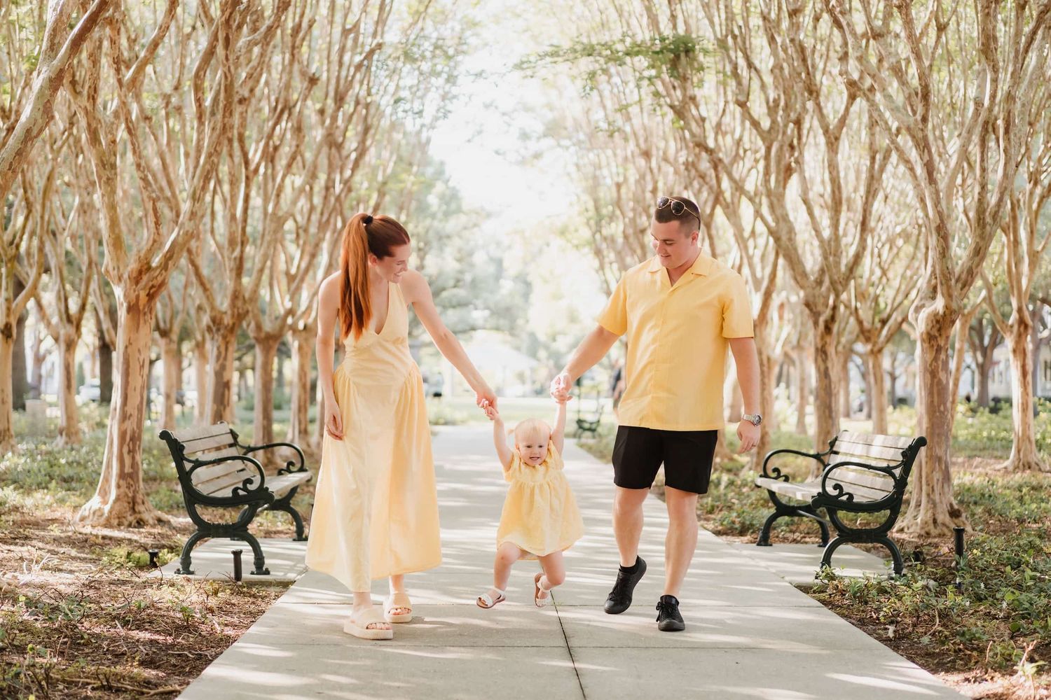 Three people in blue outfits sit together outdoors on a bench during golden hour lighting in a park setting.