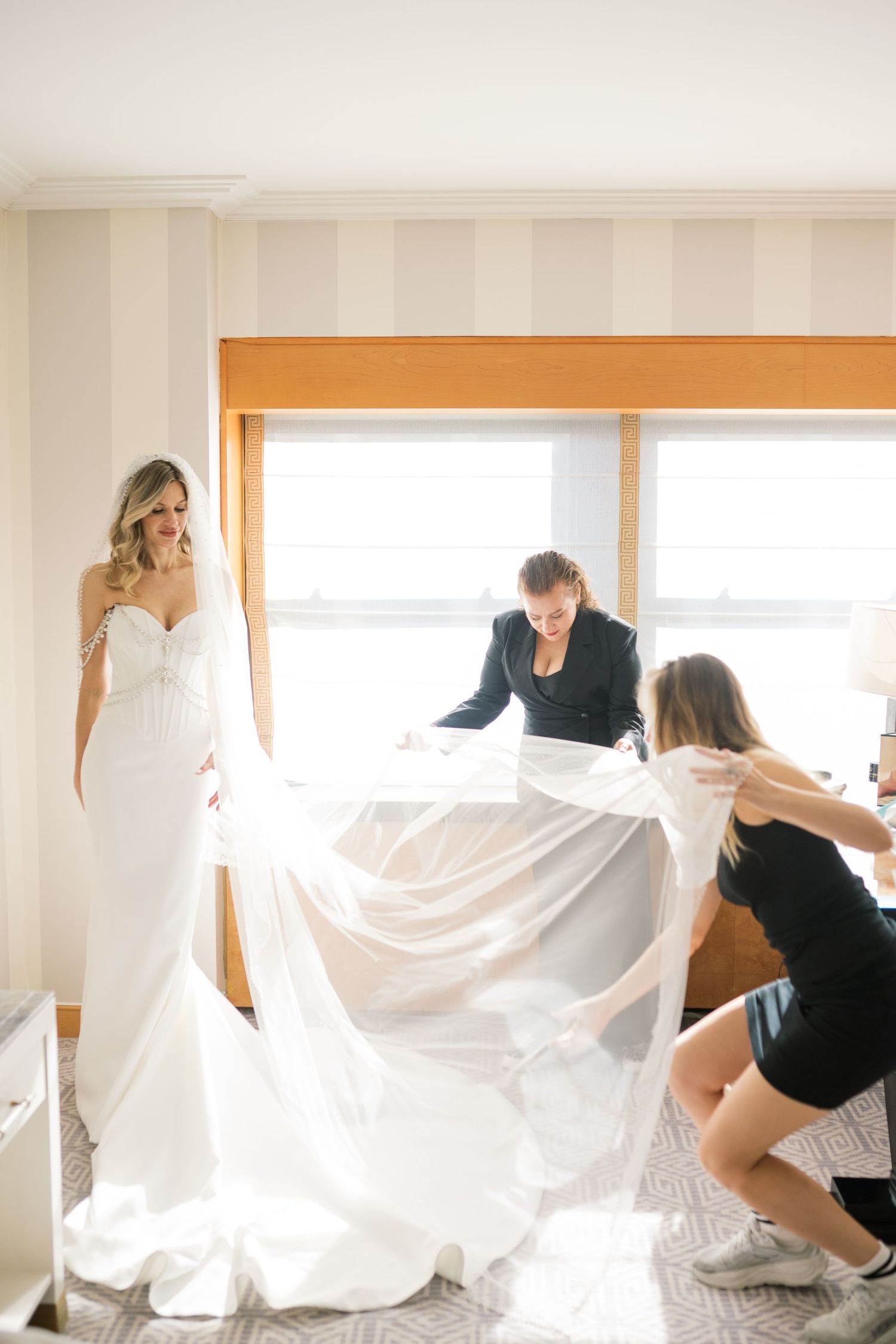 Wedding dress preparations with assistants helping to arrange the flowing white gown.