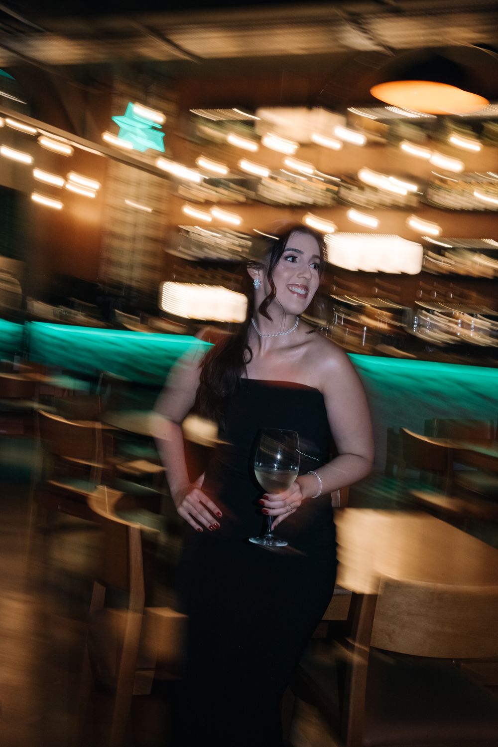 Motion blurred nightclub scene with black dress and wine glass against turquoise and amber lighting.