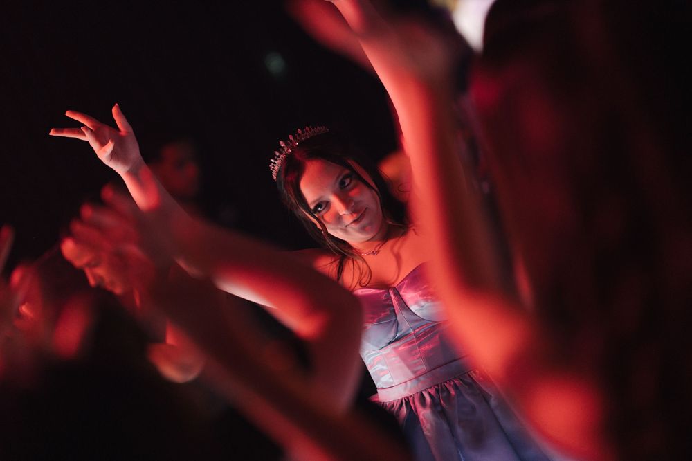 Concert crowd silhouettes raise hands in the air under dramatic red lighting during a live music performance.