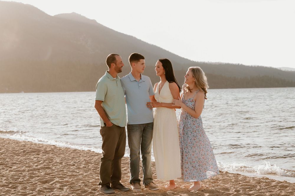 Family of four smiling together on a sandy beach with a mountain lake at golden hour.