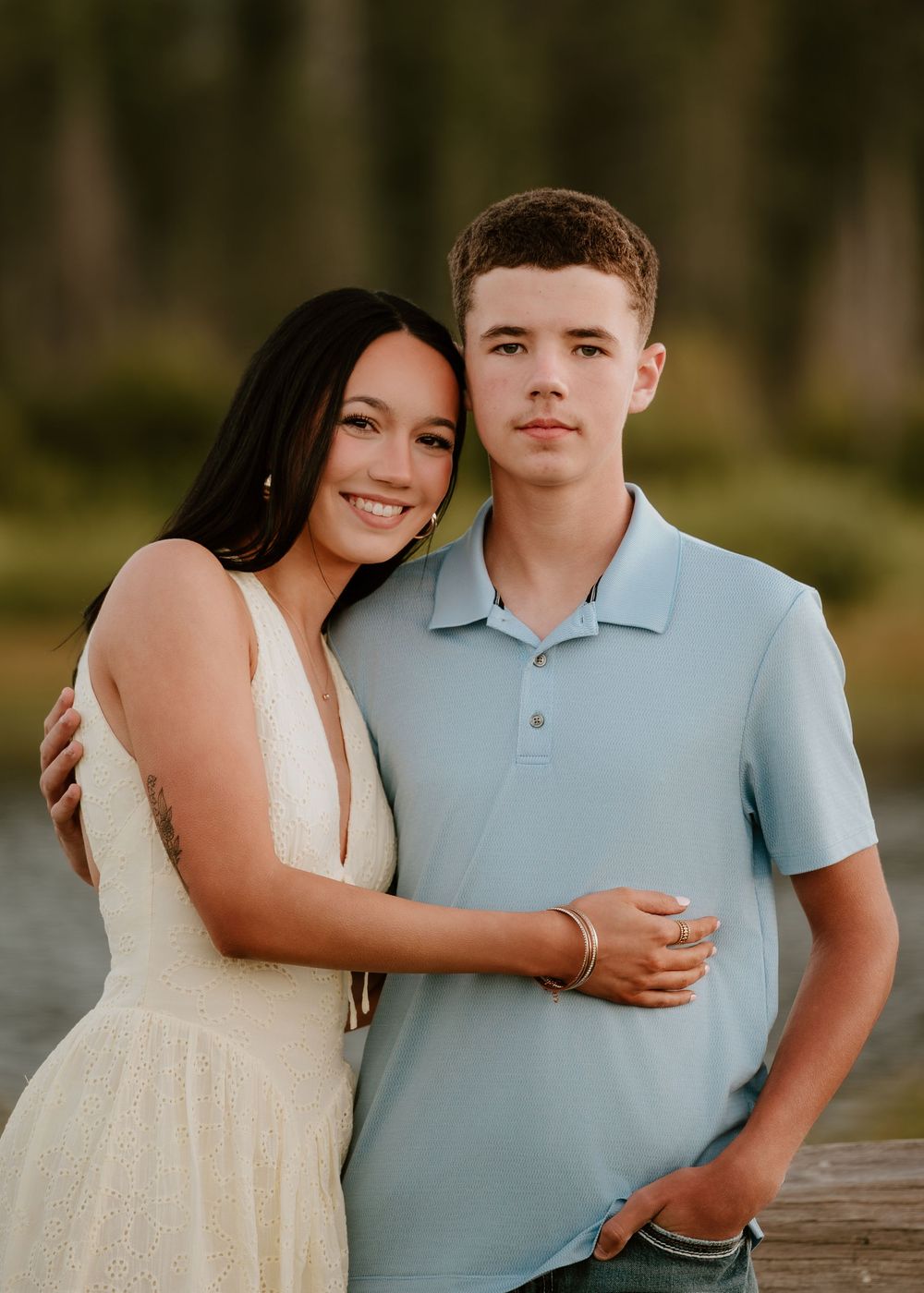 Young couple smiling and embracing outdoors near water with a softly blurred green background.