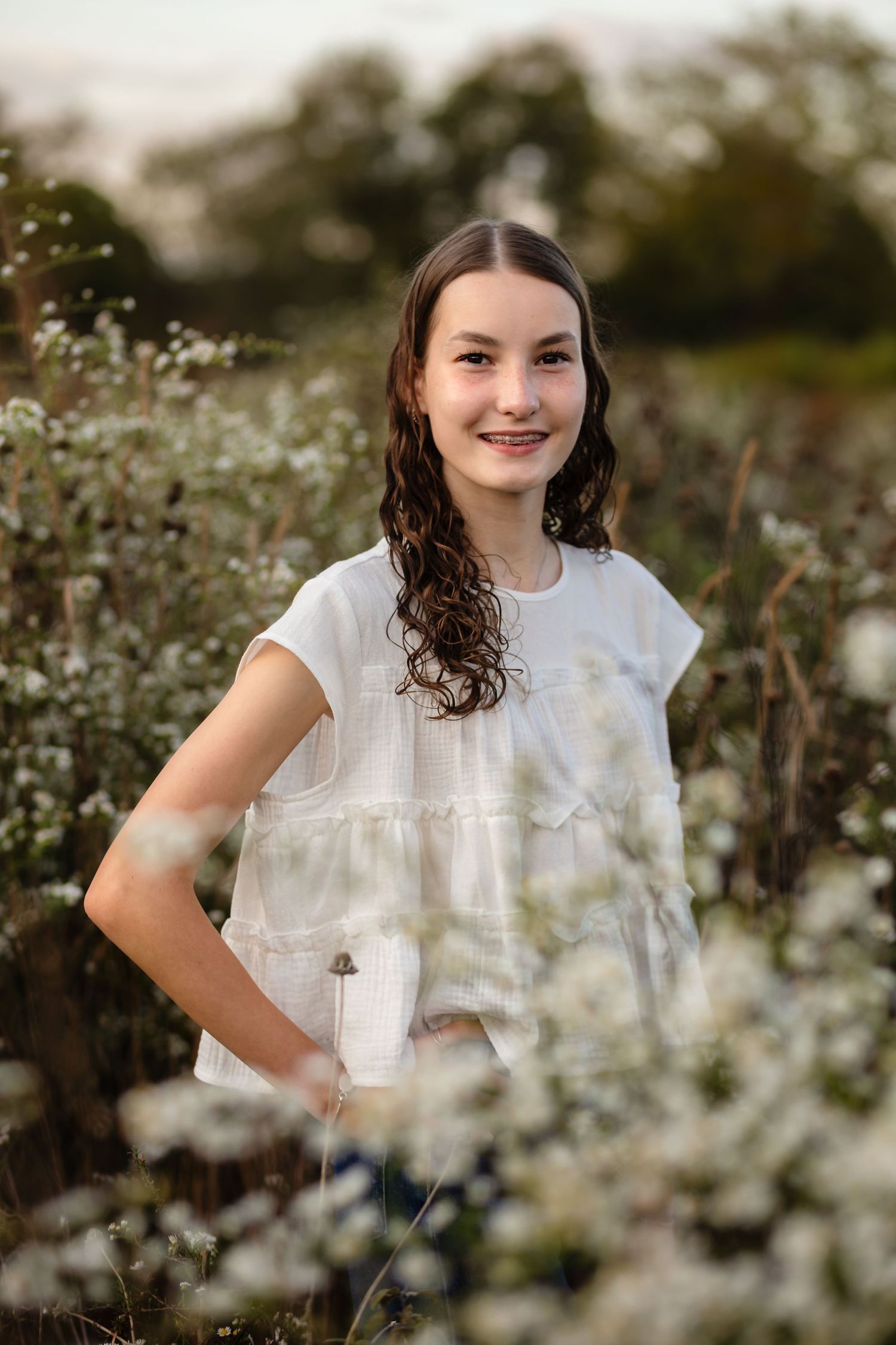 Brunette young lady in soft white smiles in a field of soft white flowers, by Charlottesville senior, family, and newborn photographer.