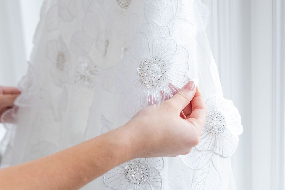 Close-up of hands adjusting a white floral embroidered bridal gown with pearl beaded accents.