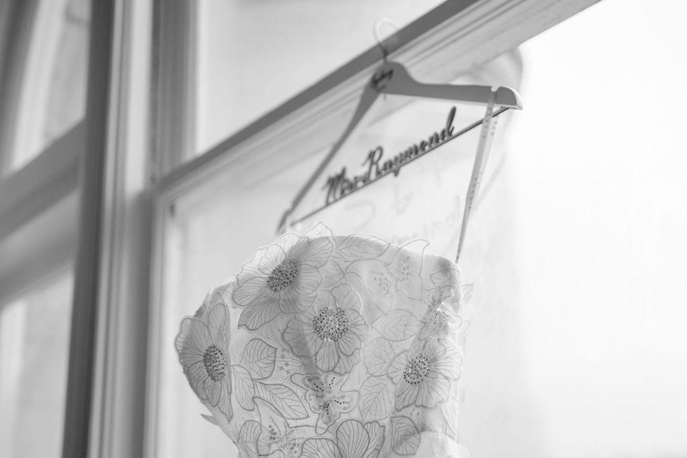 Black and white photo of a wedding dress on a personalized Mrs. Raymond hanger displayed in a window.