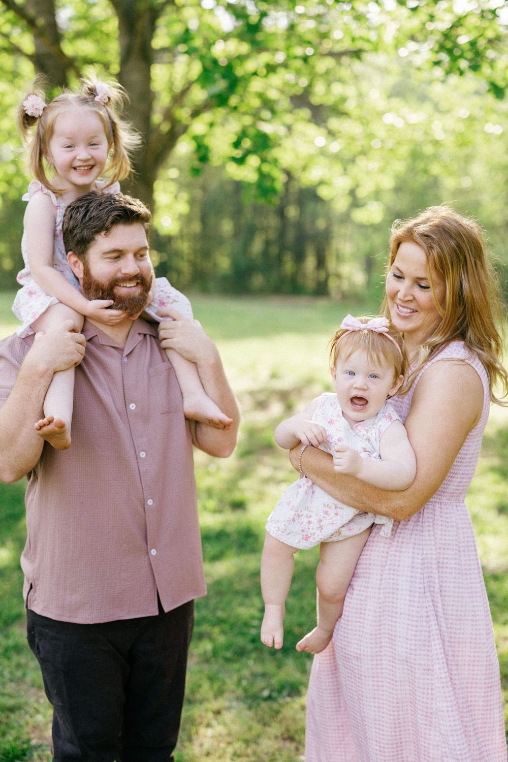 Happy family with two young daughters enjoying a sunny day outdoors in a lush green park setting.