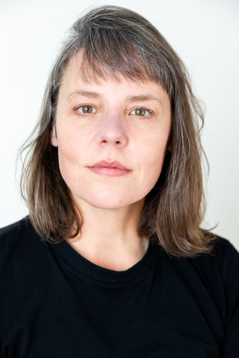 Middle-aged woman with shoulder-length gray-brown hair wearing a black t-shirt against a white background.