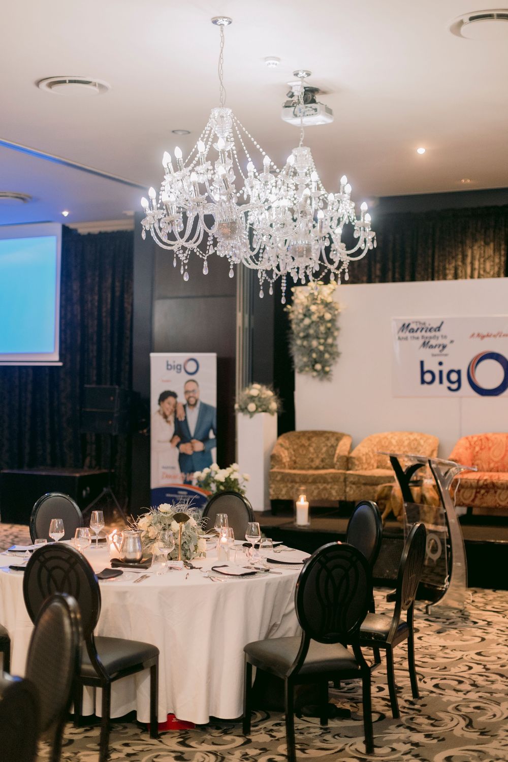 Elegant banquet hall with crystal chandelier, round tables, and Big O wedding event signage in the background.
