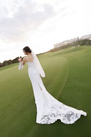Bride in elegant white lace train wedding gown standing on lush green golf course.