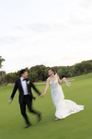 Bride and groom joyfully running hand-in-hand across a green golf course on wedding day.