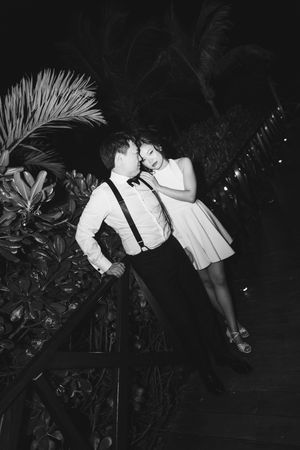 Black and white romantic photo of couple embracing near tropical palms at night.