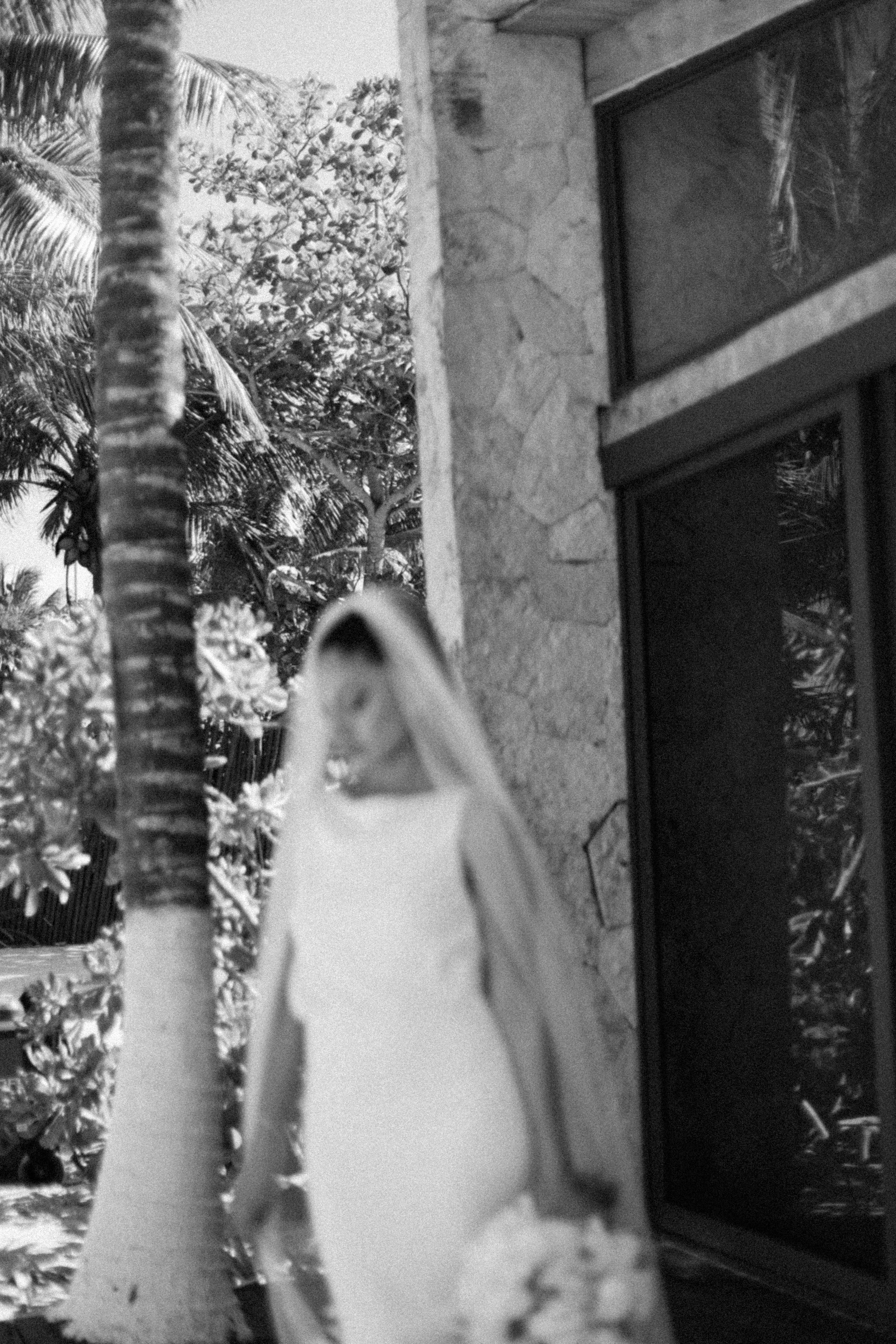 Black and white artistic blur of bride in veil near tropical stone building.