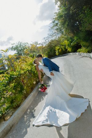 Groom dipping bride in white gown for a kiss on a curved outdoor walkway.