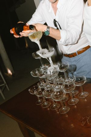 Man in white shirt pouring champagne into elegant crystal glass tower at a celebration event.