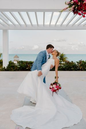 Groom in blue suit dipping bride in white gown for a kiss by the ocean.