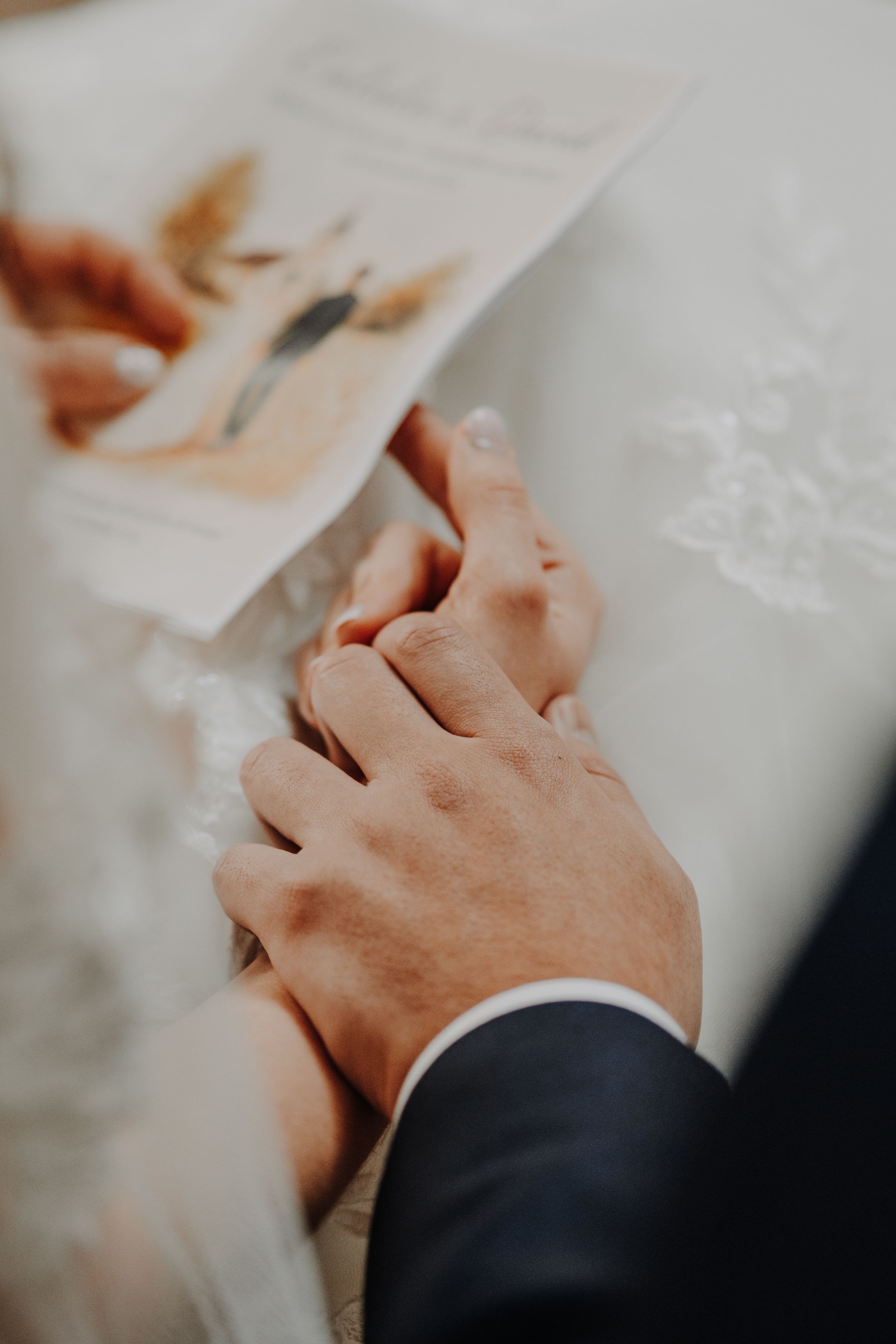 Close-up of a couple holding hands at a wedding ceremony, with a photo and white lace tablecloth in the background.