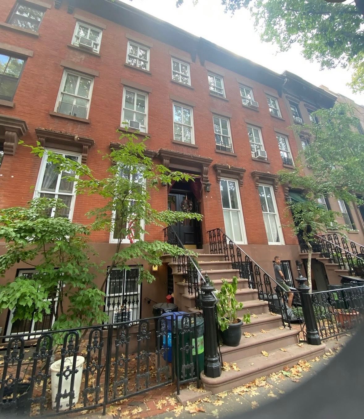 Classic red brick Brooklyn brownstone townhouses with stoops, iron railings, and lush green trees lining a quiet NYC street.