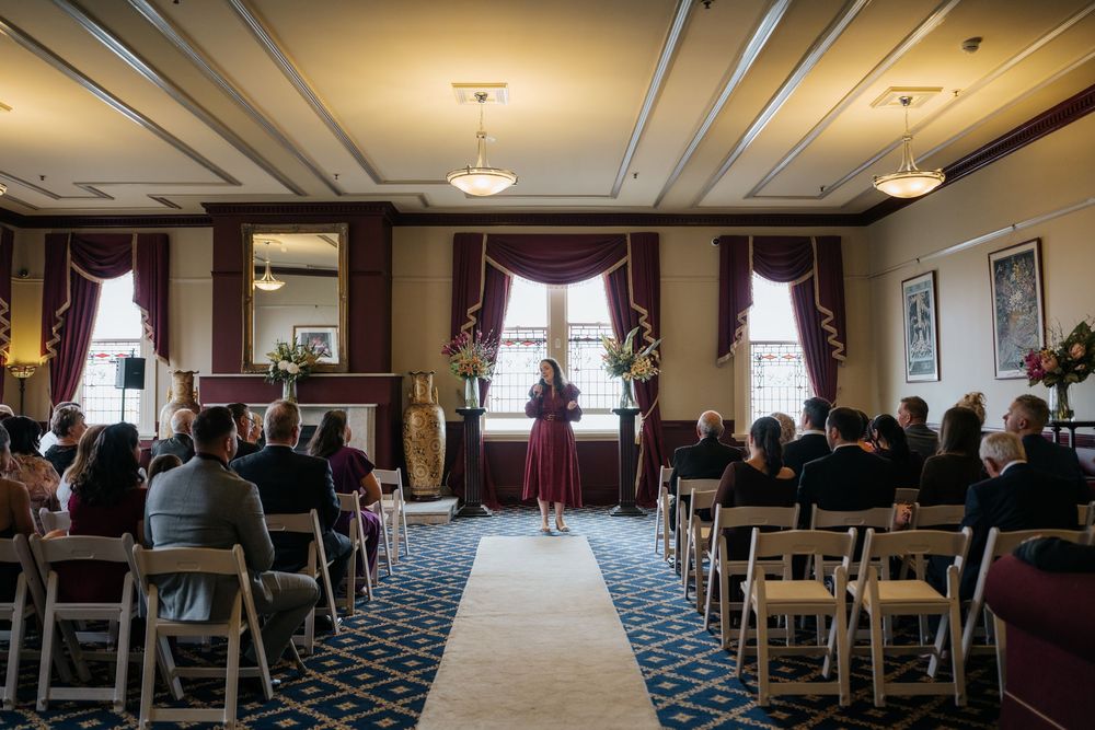 Elegant indoor wedding ceremony with guests seated in white chairs facing officiant in burgundy dress.