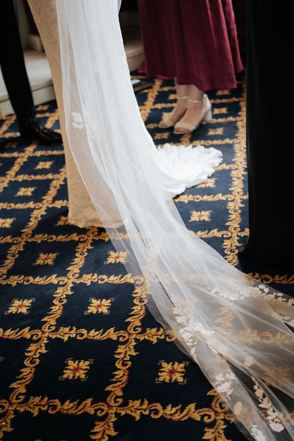 Close-up of bridal veil train flowing over ornate blue and gold patterned carpet at wedding ceremony.
