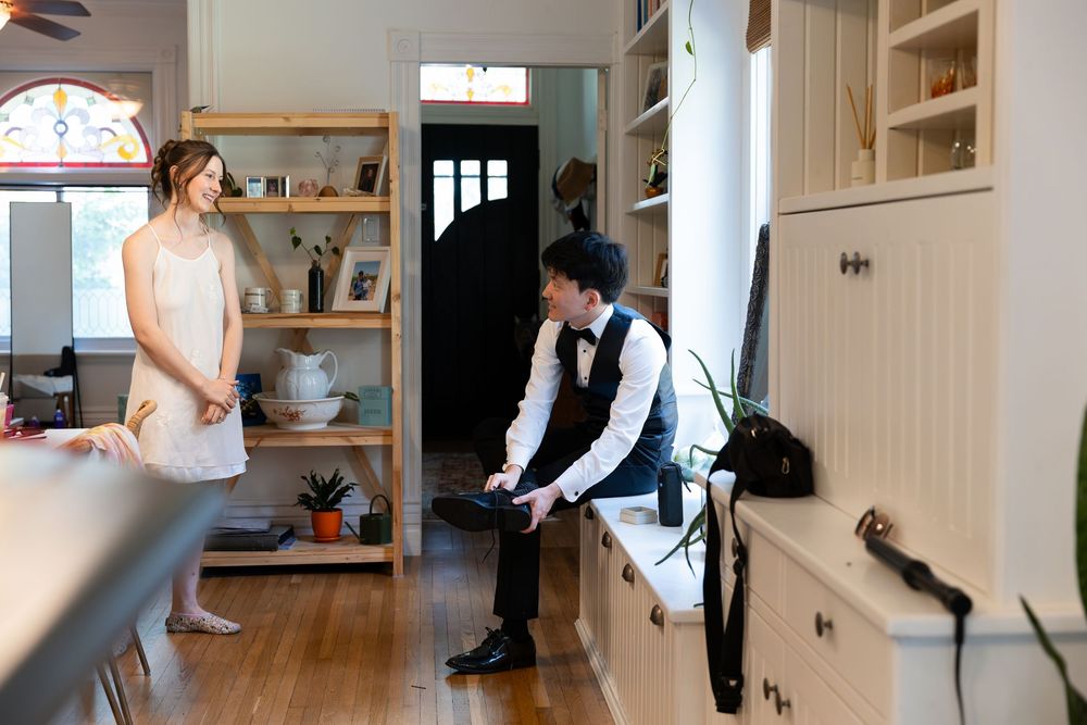 A bride in a nightgown on the morning of her wedding looks at her fiance sitting on a bench by a window in their home in London, Ontario.
