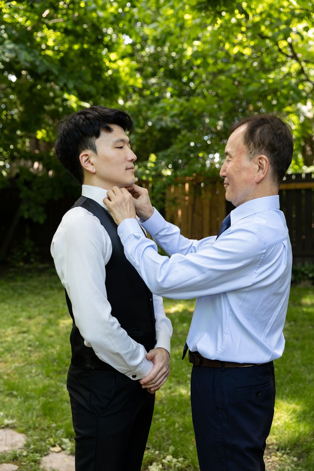 Groom getting his bow tie adjusted by his dad on the morning of his wedding in the backyard of his home in London, Ontario.