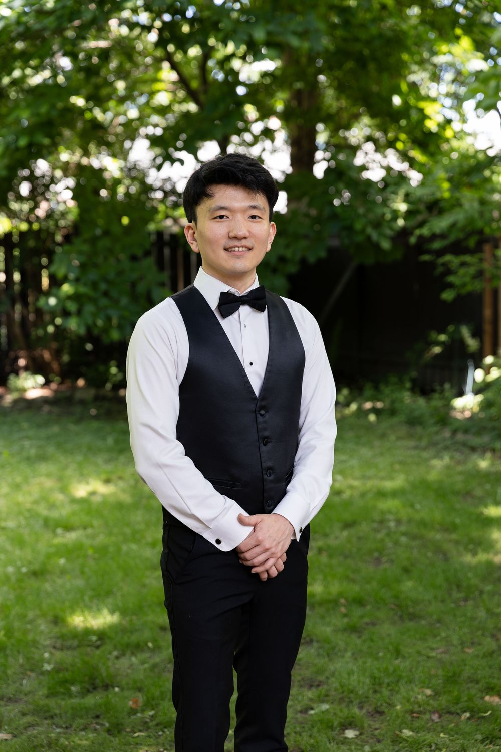 Groom standing in his vest and bowtie in the backyard of his home on the morning of their london, ontario wedding.